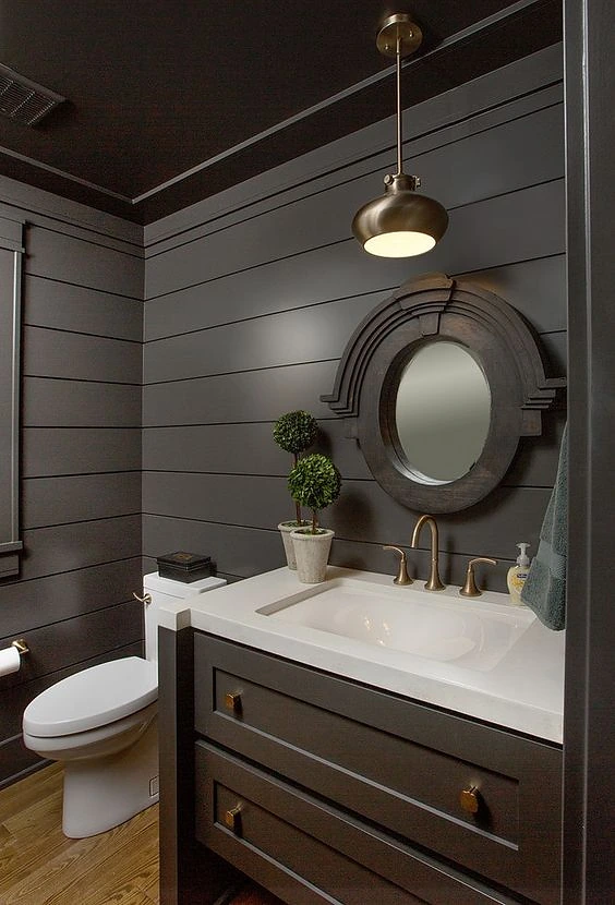 Bath with charcoal shiplap walls, a round mirror and brass fixtures